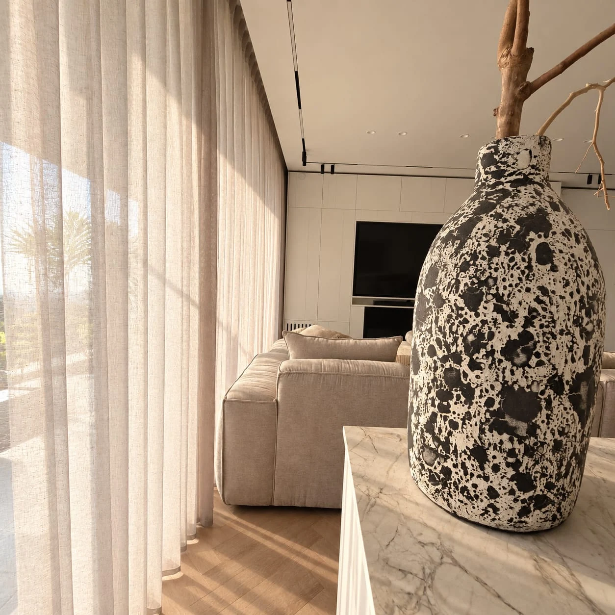 View along the sheer curtains towards the sofa and a vase on the kitchen island