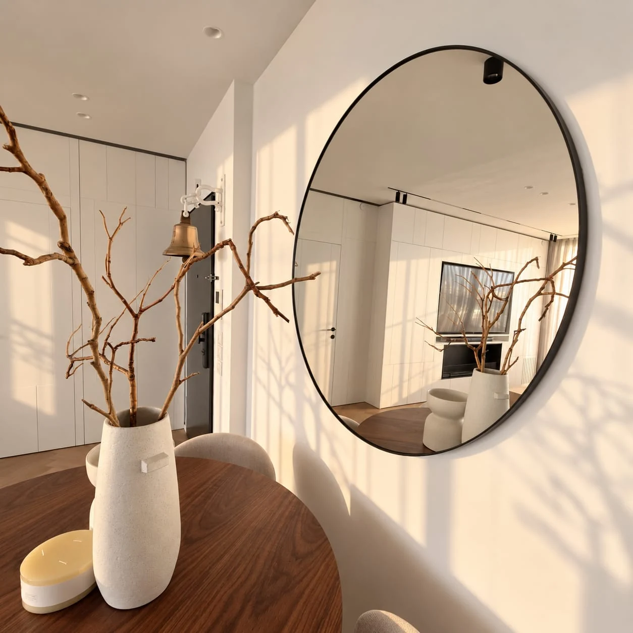 White vase and branches on the dining table beside the round mirror