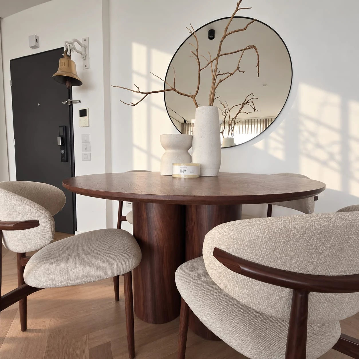 Upholstered chairs around the dark dining table beside a circular mirror