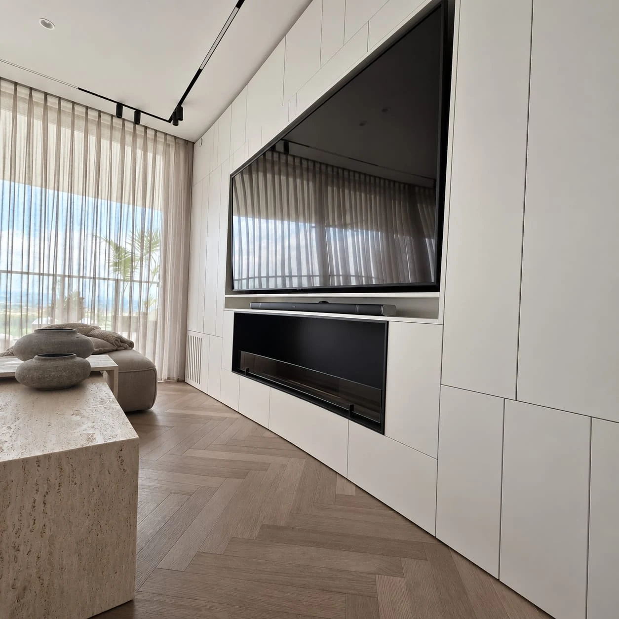 Television wall integrated into pale cabinetry beside a curtained window